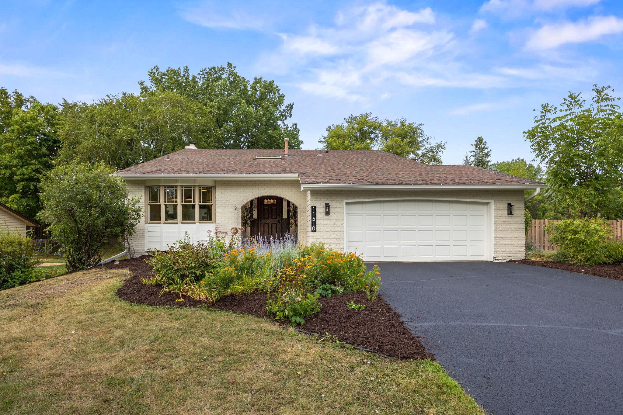 Single-story white brick ranch house with a brown roof, arched entryway, two-car garage, and a landscaped front yard. [AI-generated text]
