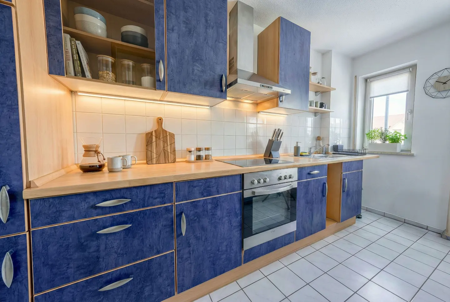 Bright kitchen with blue cabinets, light wood countertops, stainless steel appliances, and white tiled floor and backsplash.