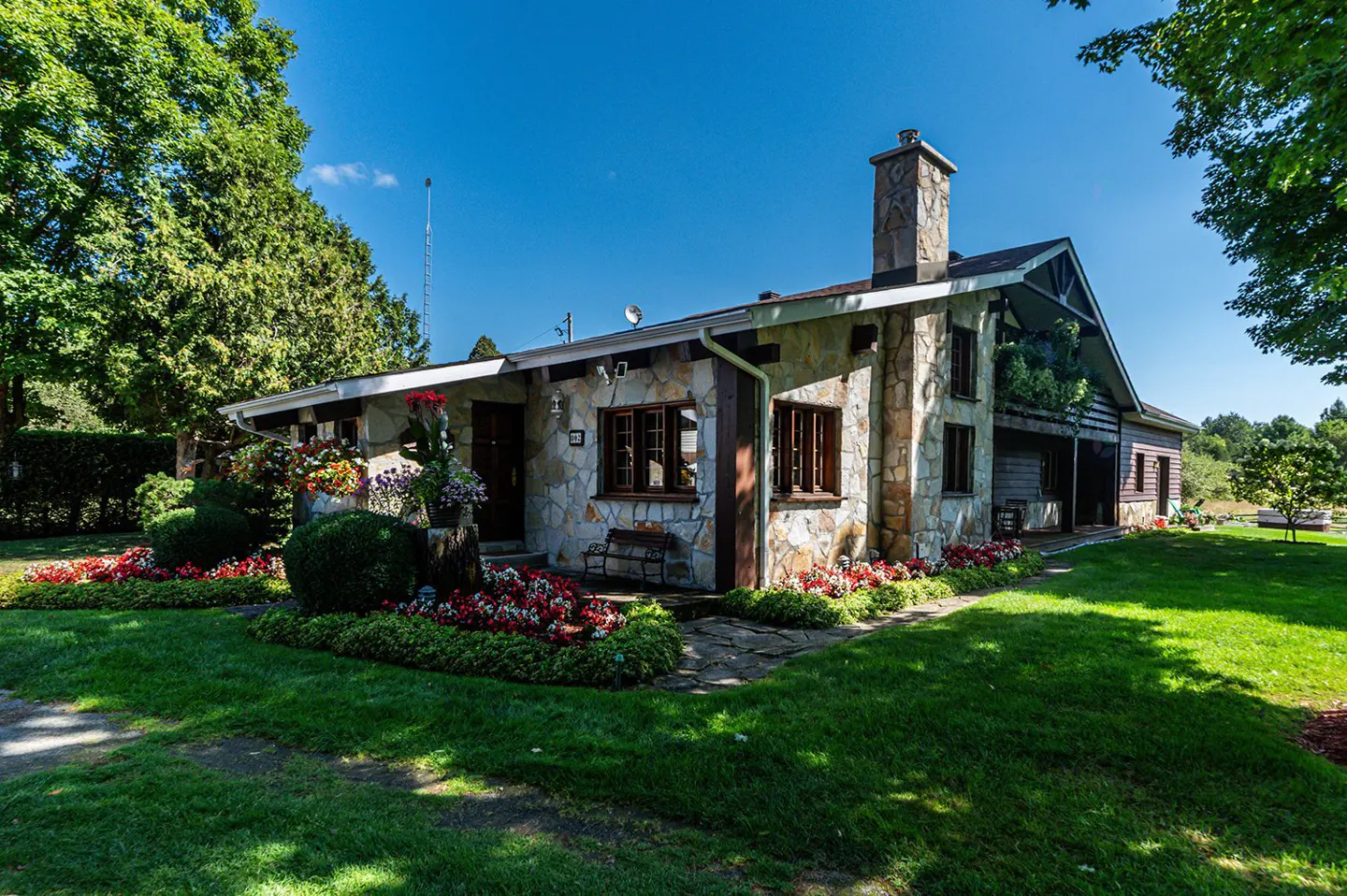 A stone house with a chimney, brown trim, and a green lawn under a blue sky.