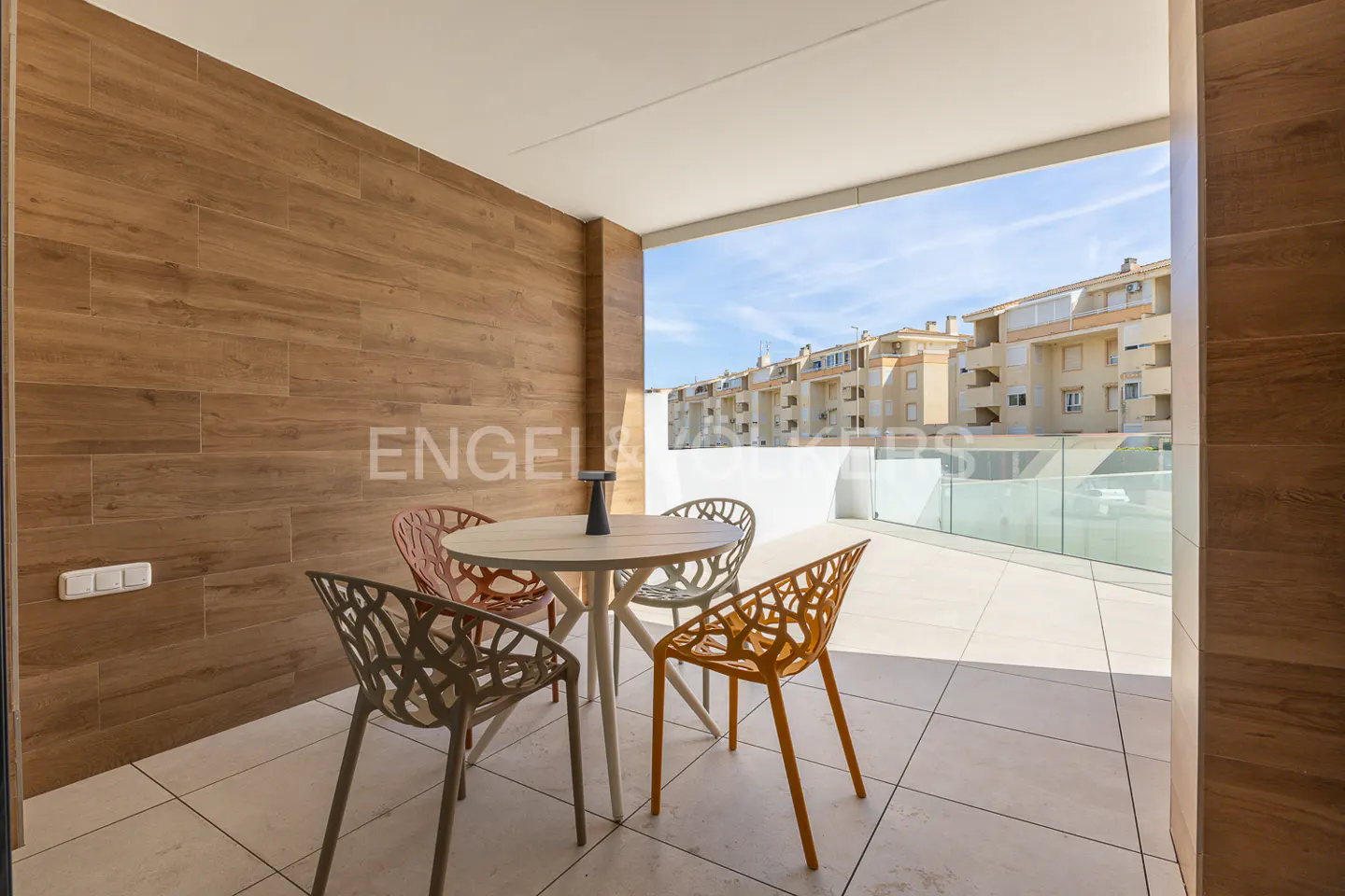 Balcony with a round table and four colorful chairs overlooking buildings under a blue sky.