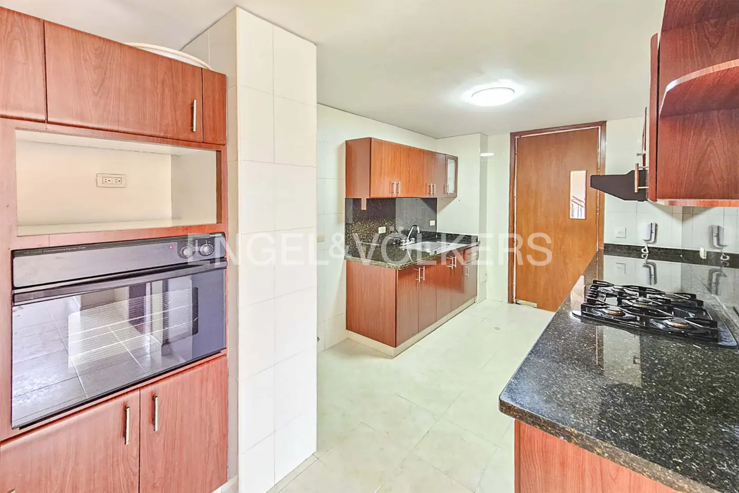 A kitchen with cherry wood cabinets, black granite countertops, and white tile floors. A black oven is built into the cabinets.