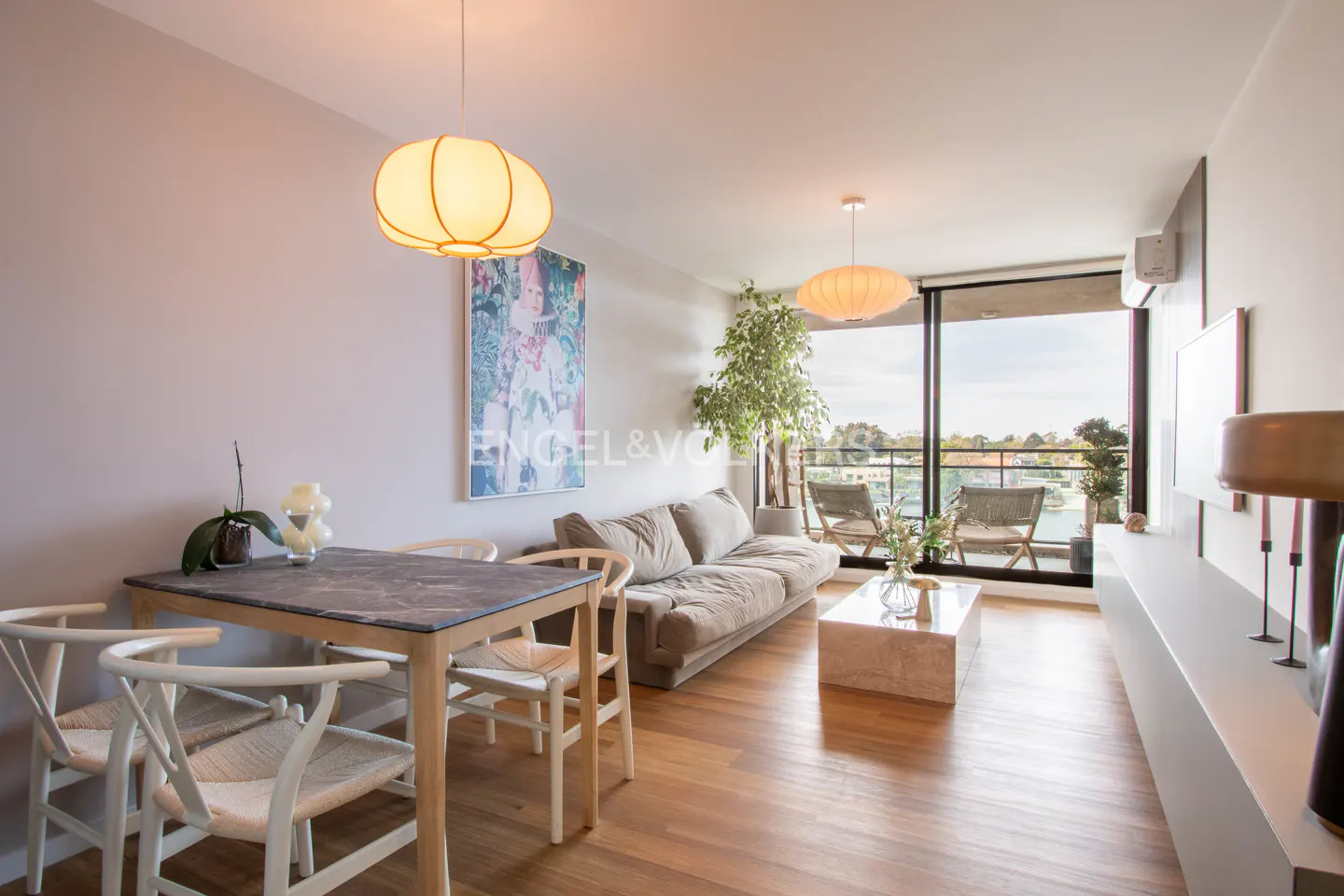A bright living room with a dining table, a beige sofa, and a balcony with a view.