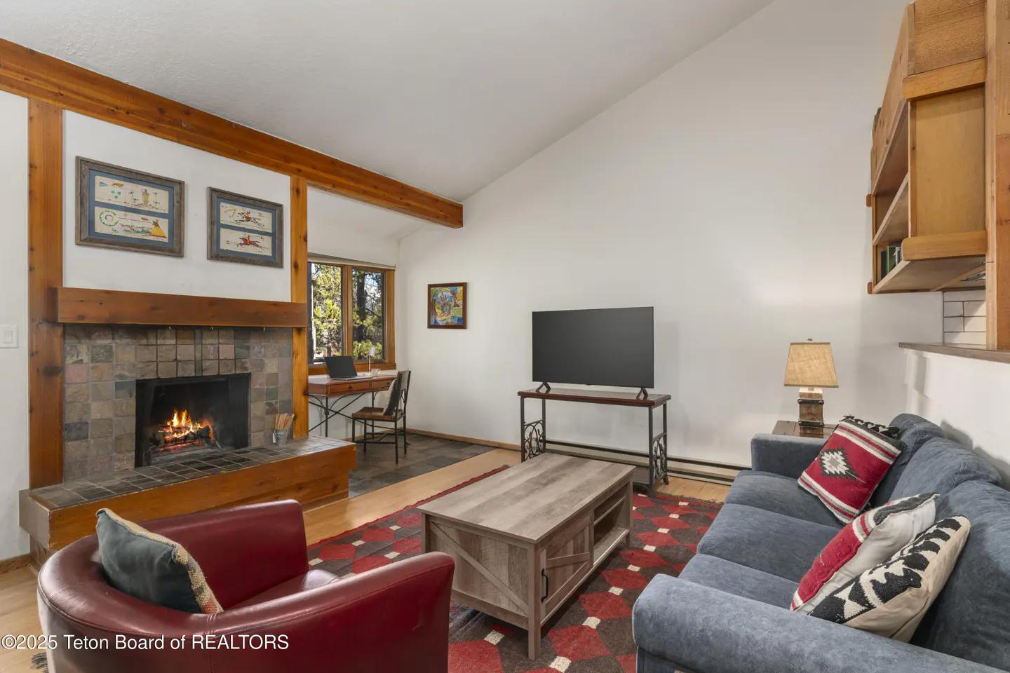 Living room with a stone fireplace, red chair, blue sofa, and a wooden coffee table on a red patterned rug.