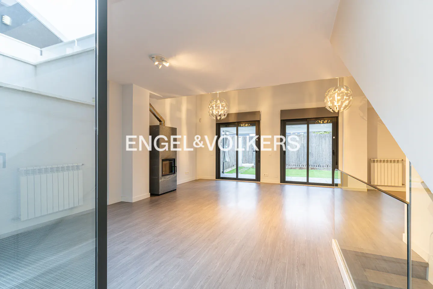 Bright, modern living room with wood floors, fireplace, and sliding glass doors to a green yard. Chandeliers hang from the ceiling.