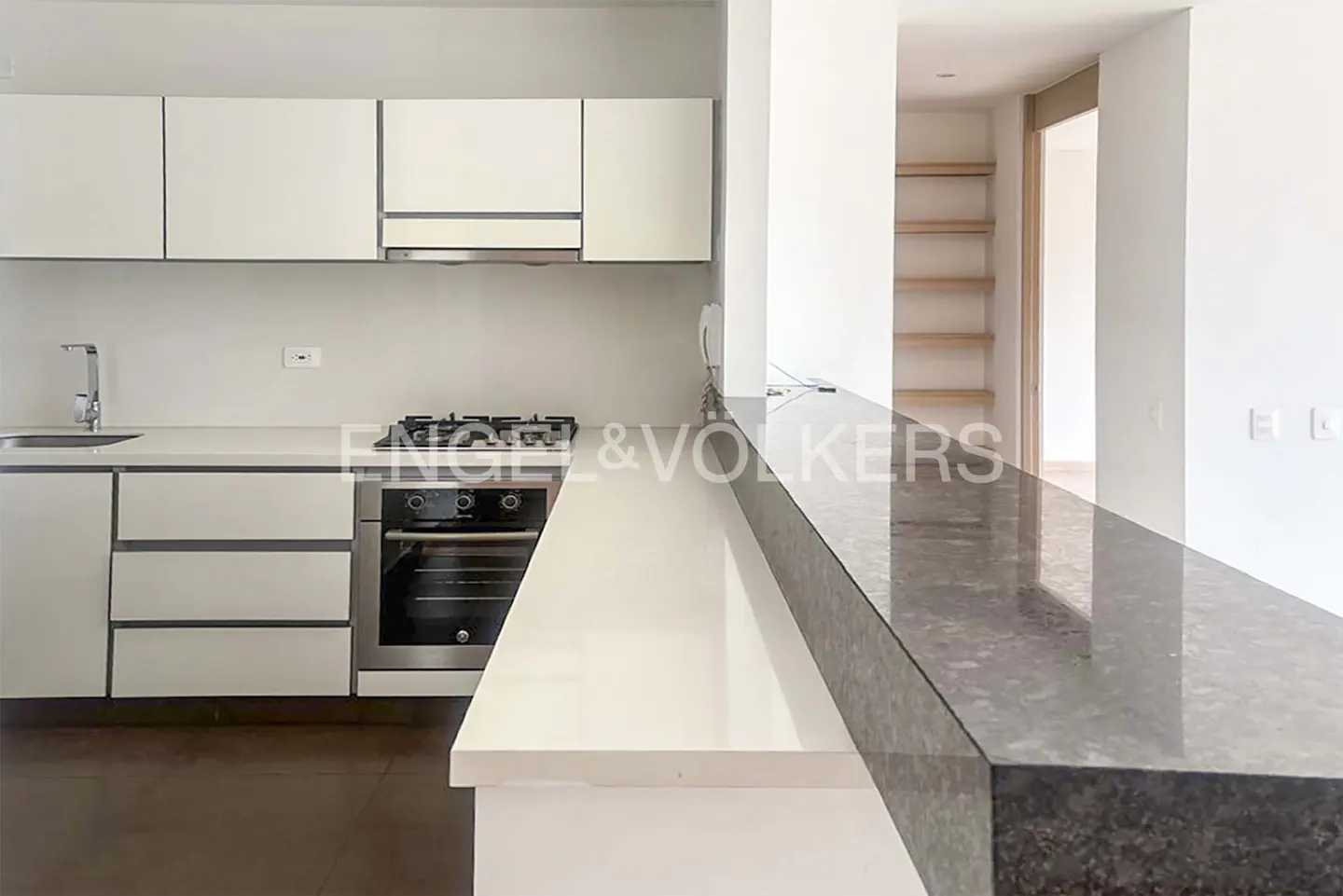A modern kitchen with white cabinets, stainless steel appliances, and a two-tone countertop. A glimpse of wooden shelves is visible in the background.