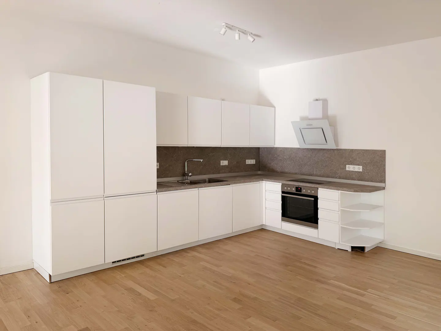 Bright, modern kitchen with white cabinets, gray countertops, and wood floors. Oven, sink, and range hood are visible.