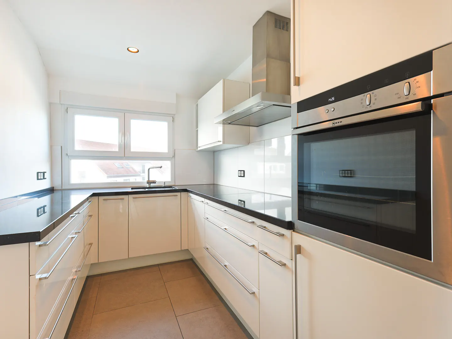 A modern kitchen with white cabinets, black countertops, stainless steel oven and range hood. A window is above the sink.
