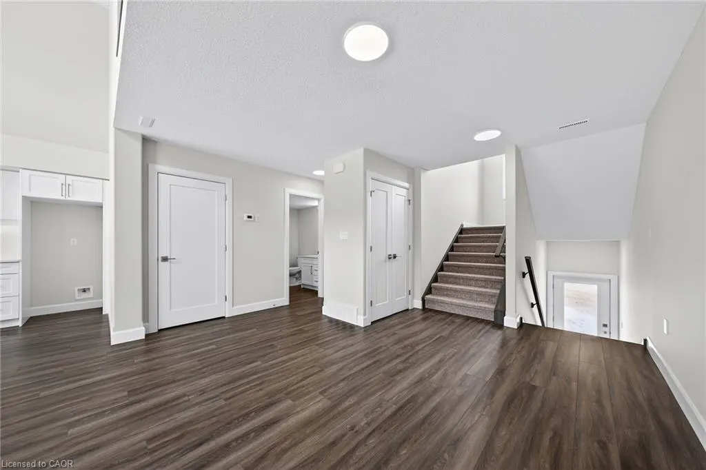 A bright, open-concept living space with dark wood floors, white walls, and recessed lighting. A staircase leads to a lower level.