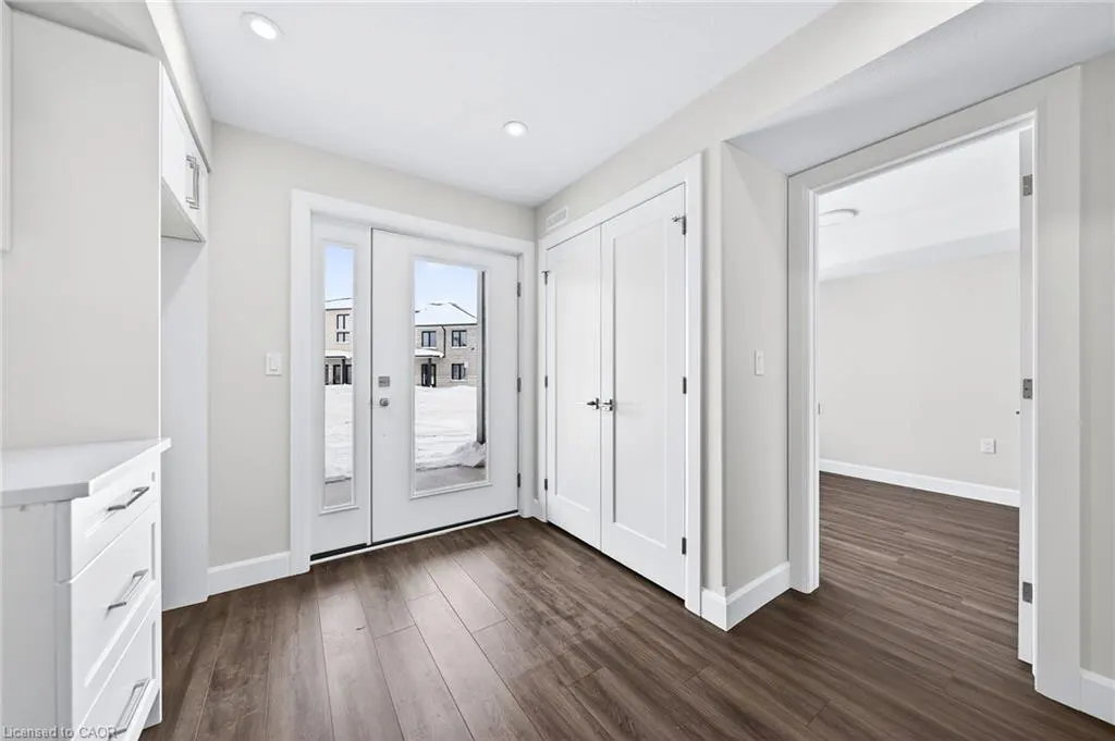 Bright entryway with dark wood floors, white walls, and white trim. A glass door leads outside to a snowy scene. A white closet and doorway are visible.