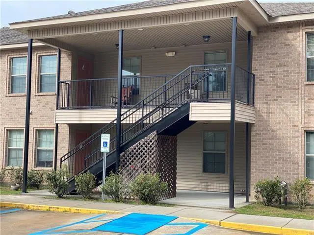 Two-story tan brick apartment building with an exterior black metal staircase leading to a second-floor balcony.