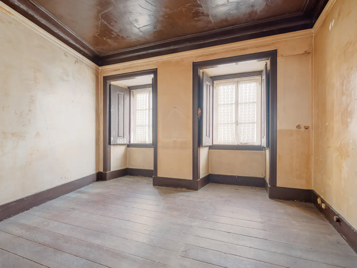 Empty room with two windows, wooden floors, and beige walls. Dark brown trim accents the windows, ceiling, and baseboards.