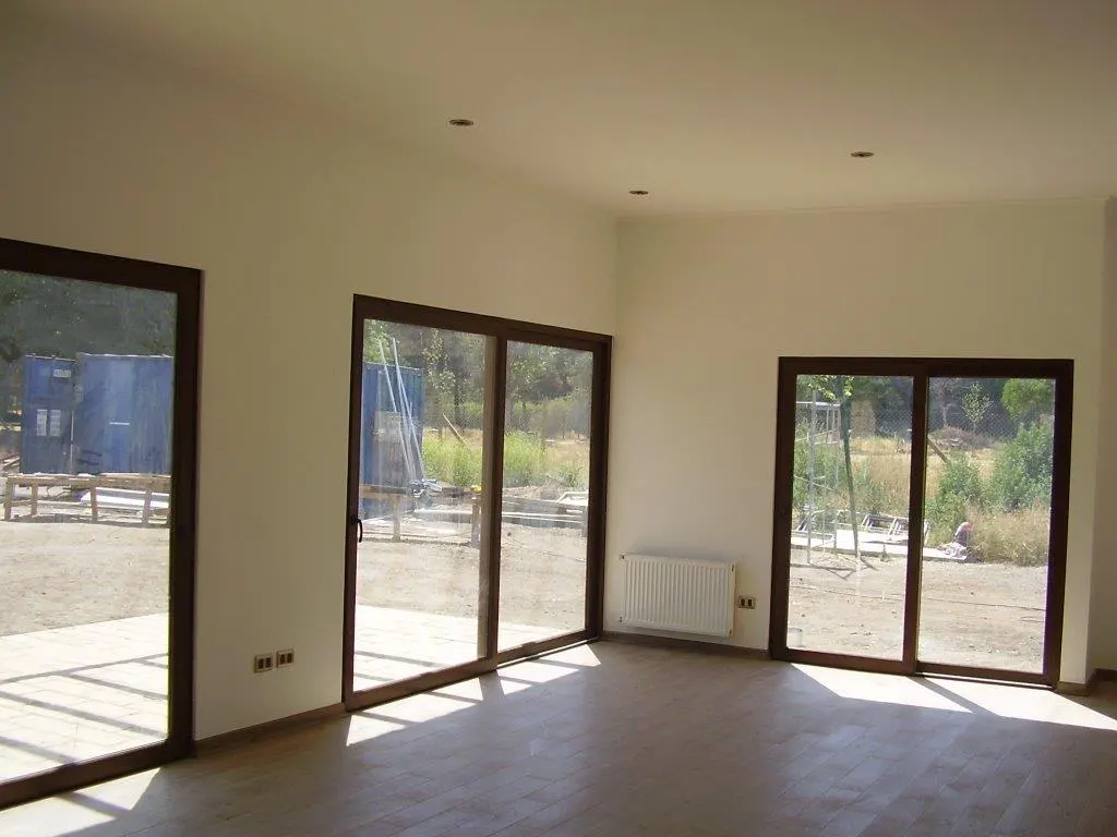 Bright, empty room with light walls, wood floors, and three large sliding glass doors with dark frames. A white radiator is on the wall.