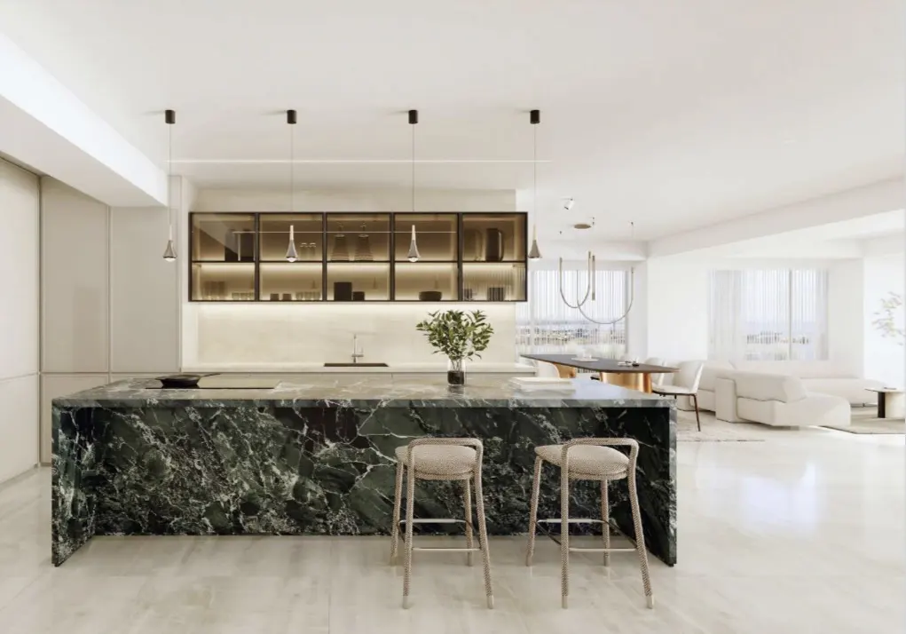 A modern, open-concept kitchen with a green marble island and two stools. Cabinets and pendant lights hang above the counter.