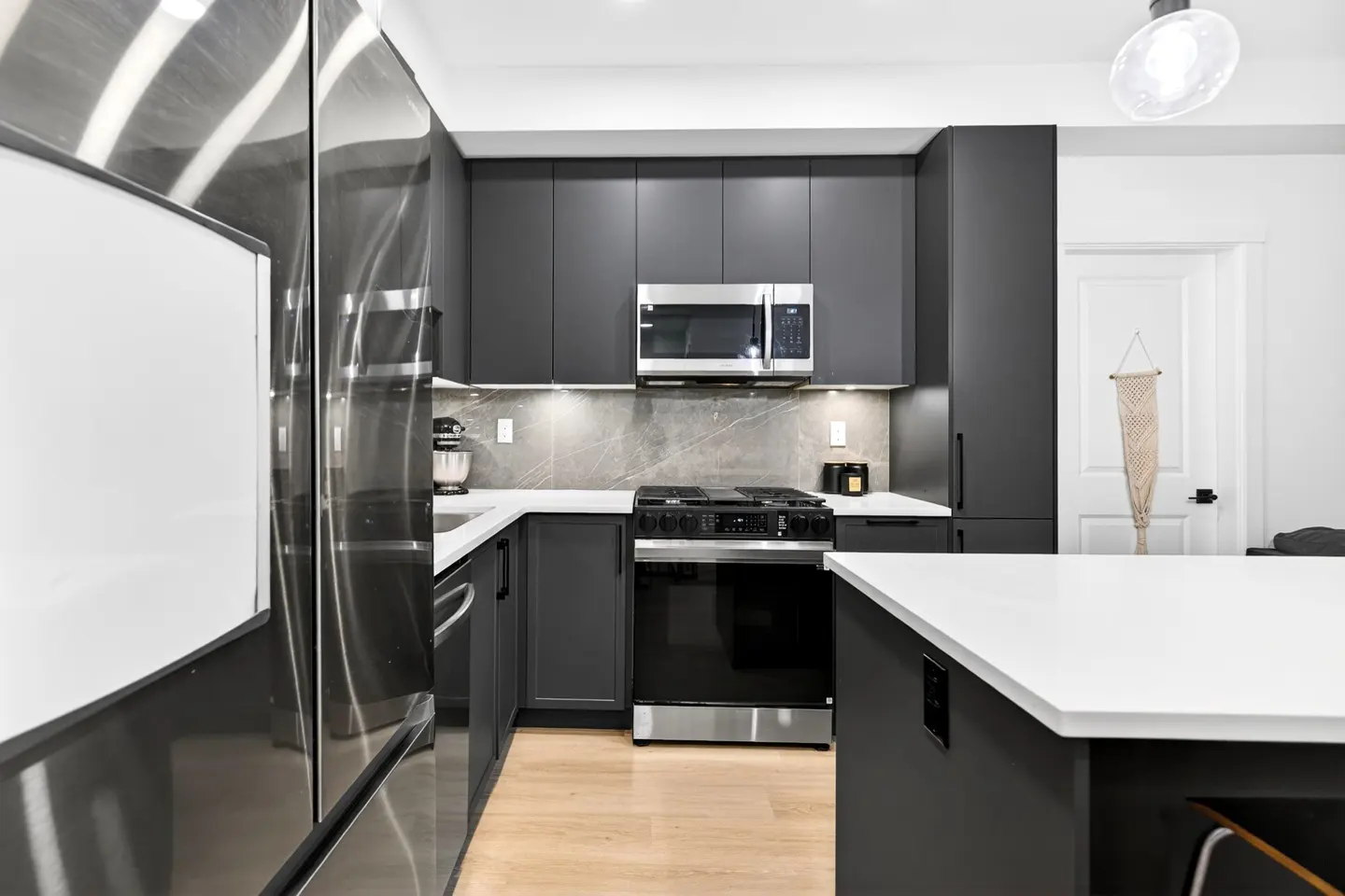 Modern kitchen with stainless steel appliances, gray cabinets, white countertops, and light wood floors.