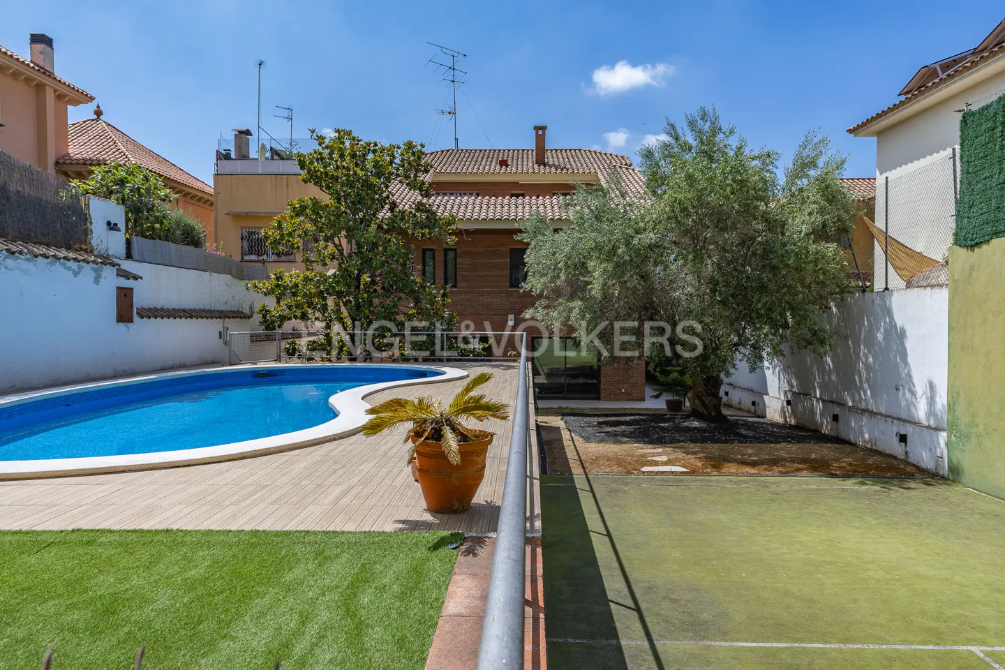 Outdoor view of a property with a blue pool, green lawn, tennis court, and trees under a sunny sky.