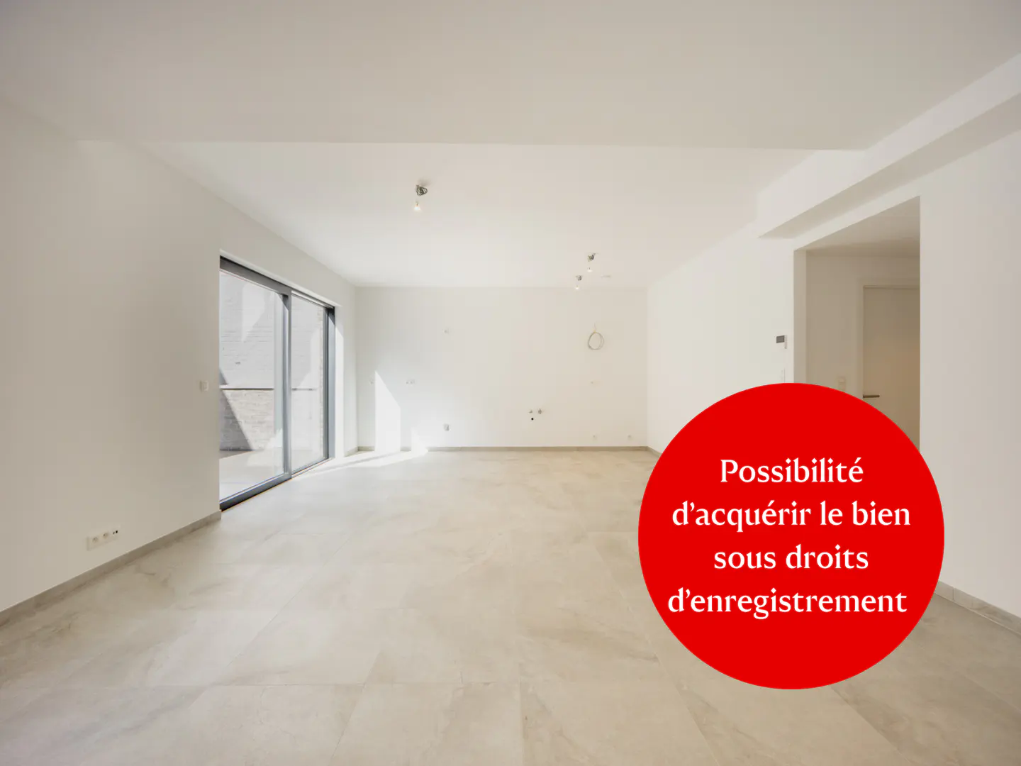 Bright, empty room with white walls, light tile floor, and sliding glass doors. A red circle with white text is superimposed on the image.