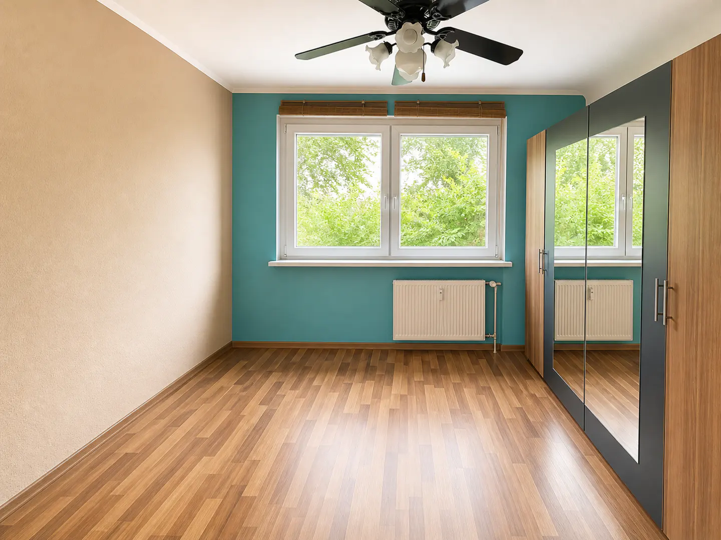 Empty bedroom with wood floors, tan and teal walls, a window with green trees outside, and a wood wardrobe with mirrored doors.