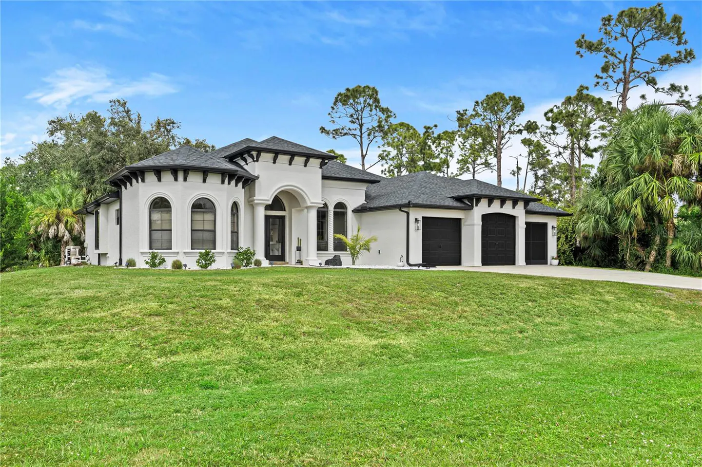 A white, single-story house with a black roof and a two-car garage sits on a green lawn under a blue sky.