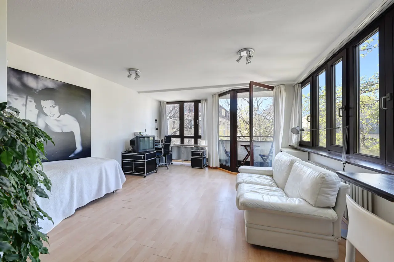 Bright living room with wood floors, white sofa, balcony, and large black and white portrait.