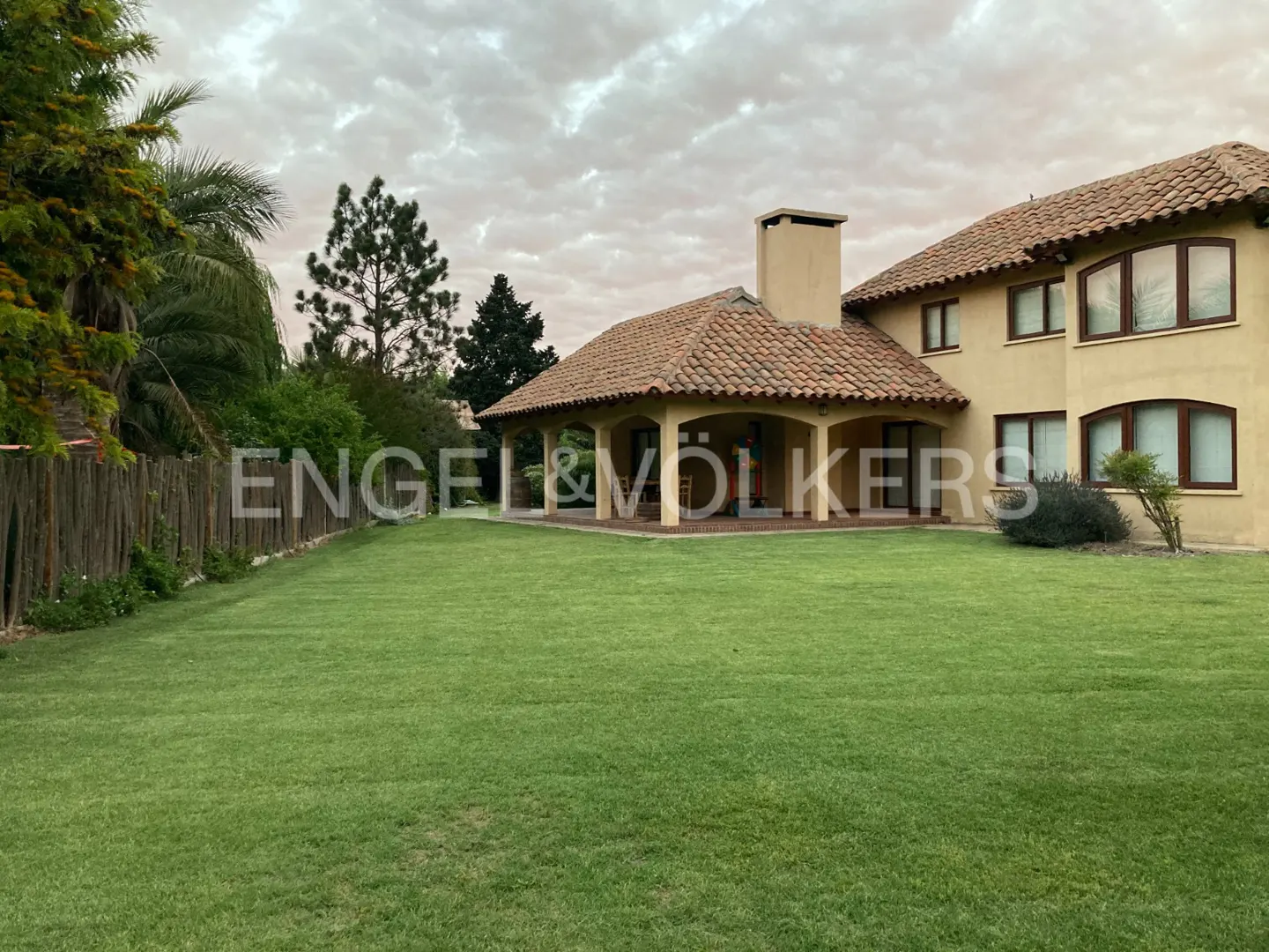 Exterior view of a tan two-story house with a red tile roof and a large green lawn.