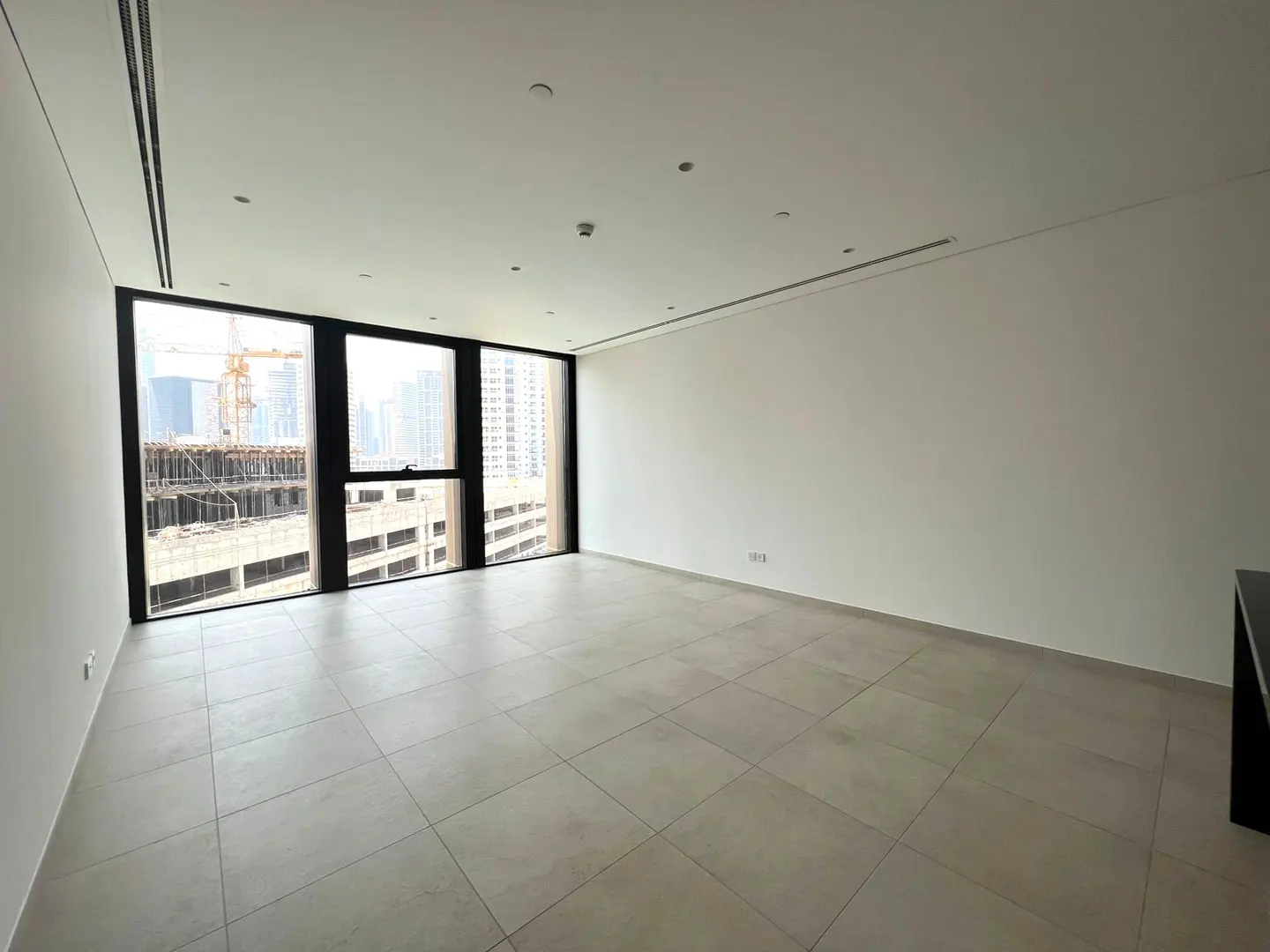 Empty, modern room with white walls, tiled floors, and large windows overlooking a city construction site.