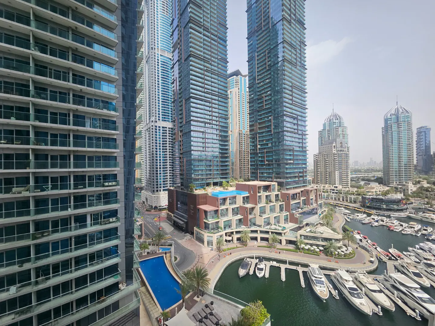 View of Dubai Marina with skyscrapers, a blue pool, and yachts docked in the harbor.