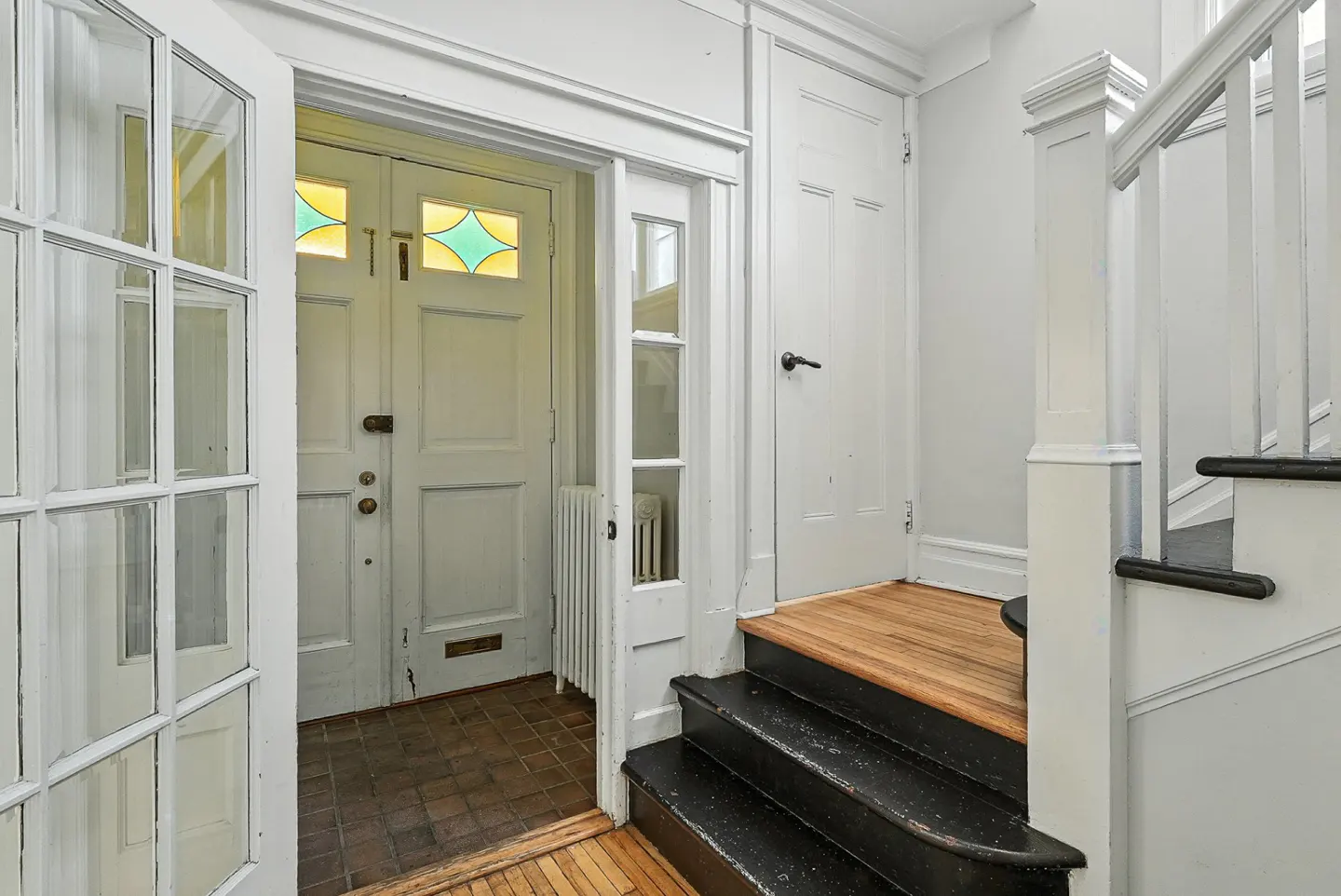 A bright foyer with white walls, black stairs, and a white door with stained glass. A glass paneled door is on the left.