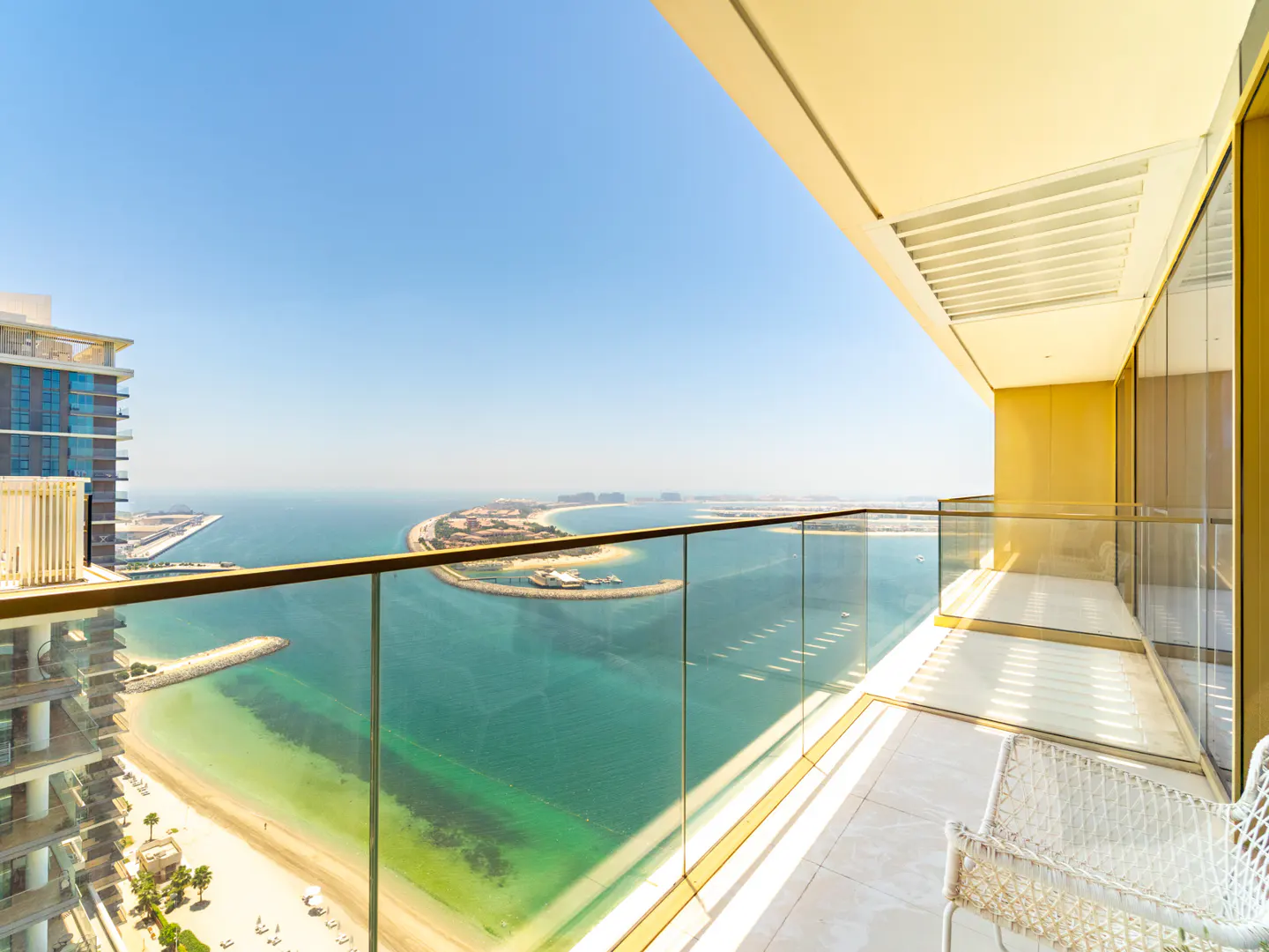 High-rise balcony with glass railings overlooking a turquoise beach, ocean, and distant island under a clear blue sky.