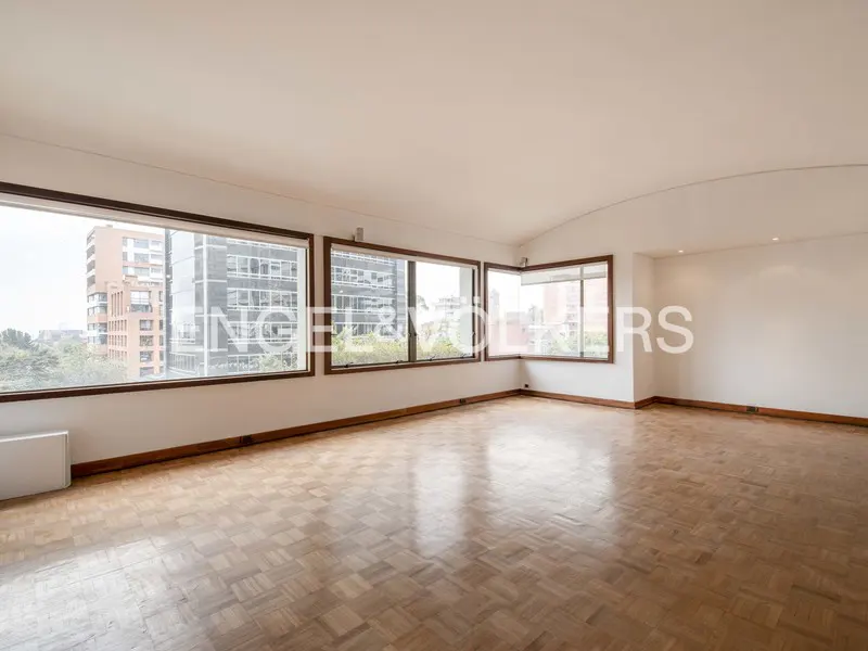 Empty room with parquet floors, white walls, and large windows with city views.