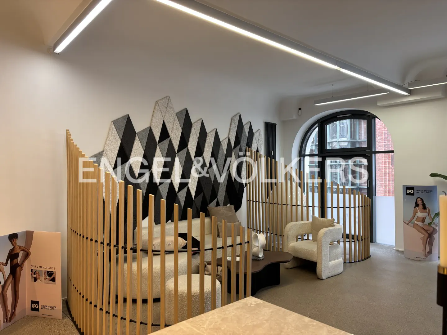 Engel & Volkers office interior with a modern design. A seating area with a sofa, chair, and wooden accents. Black and white geometric wall decor.