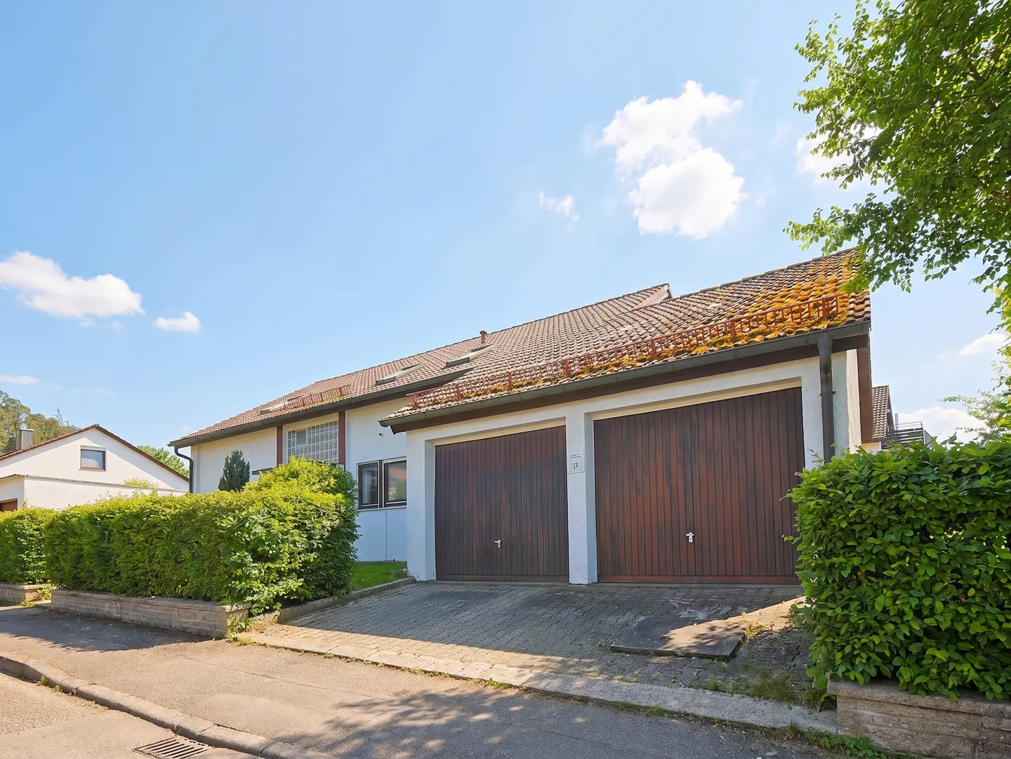 Two-car garage with brown doors and a white exterior, set against a blue sky with green foliage.