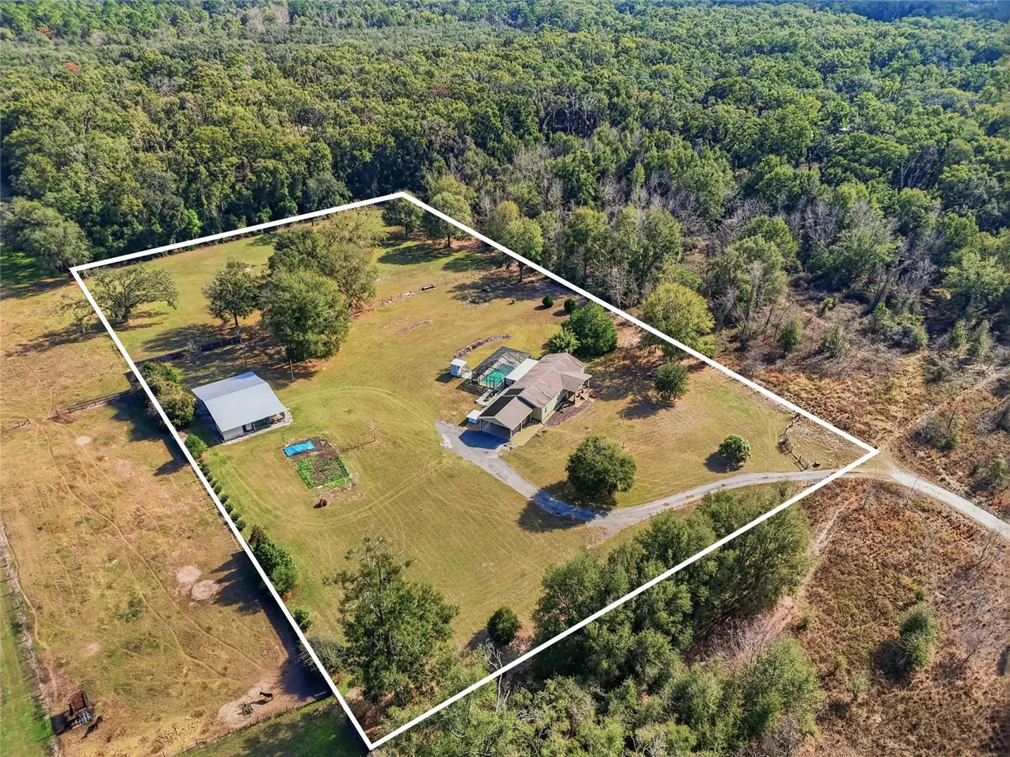 Aerial view of a property with a house, pool, barn, and garden, outlined in white, surrounded by trees.