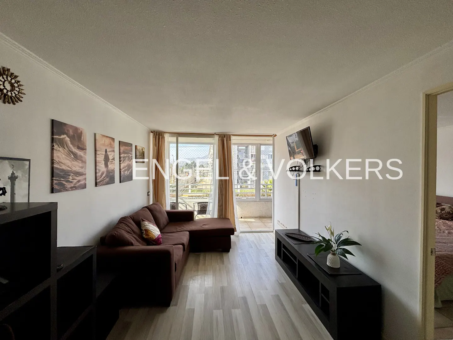 Living room with brown sectional sofa, black shelving, and wall art. Balcony with city view in background.