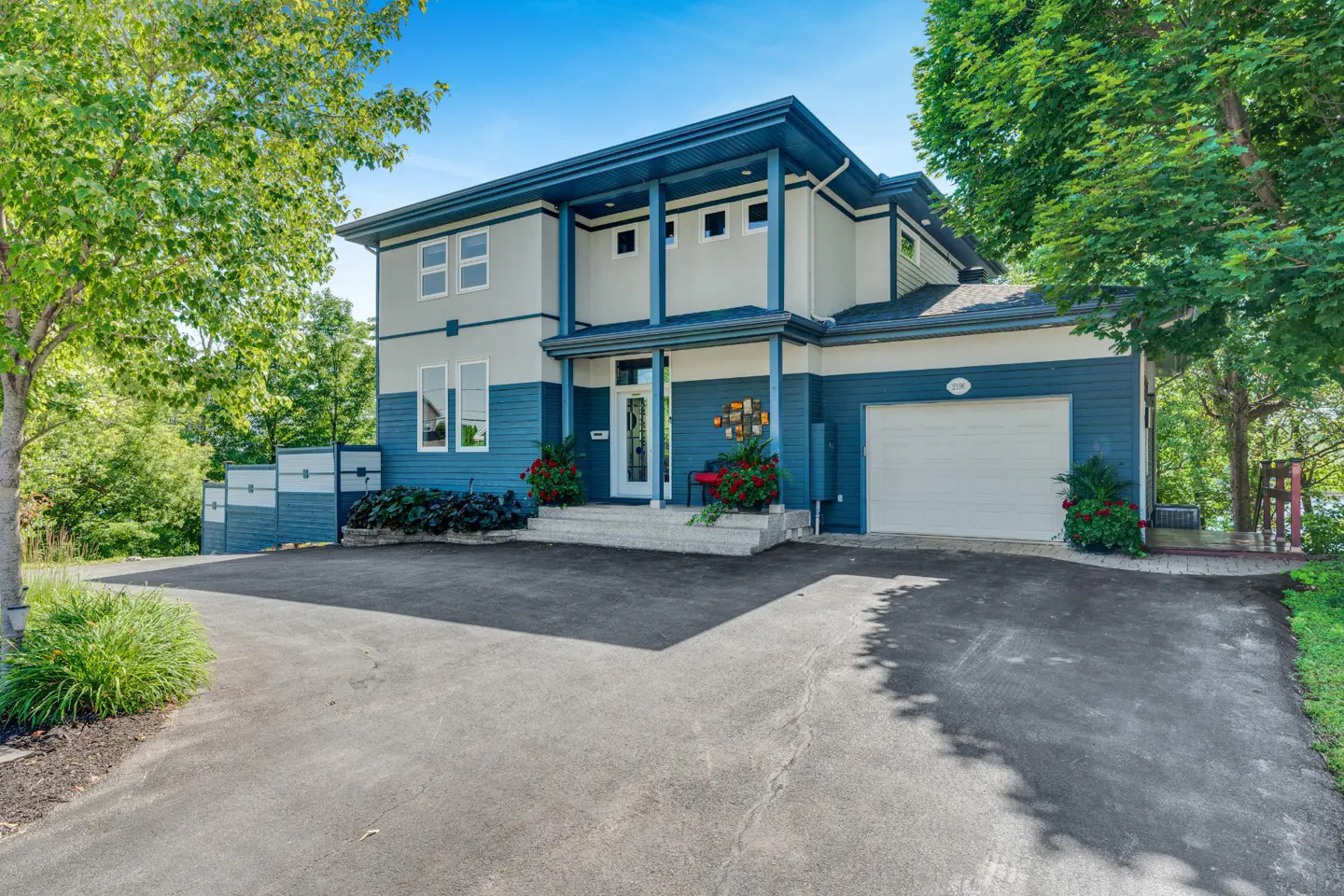 Two-story house with blue and gray siding, white trim, and a white garage door. A paved driveway leads to the house.