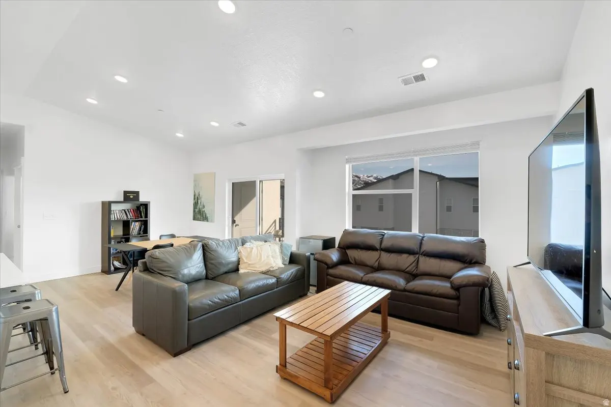 Bright living room with two leather sofas, a wooden coffee table, and a large TV. A window shows a view of mountains.