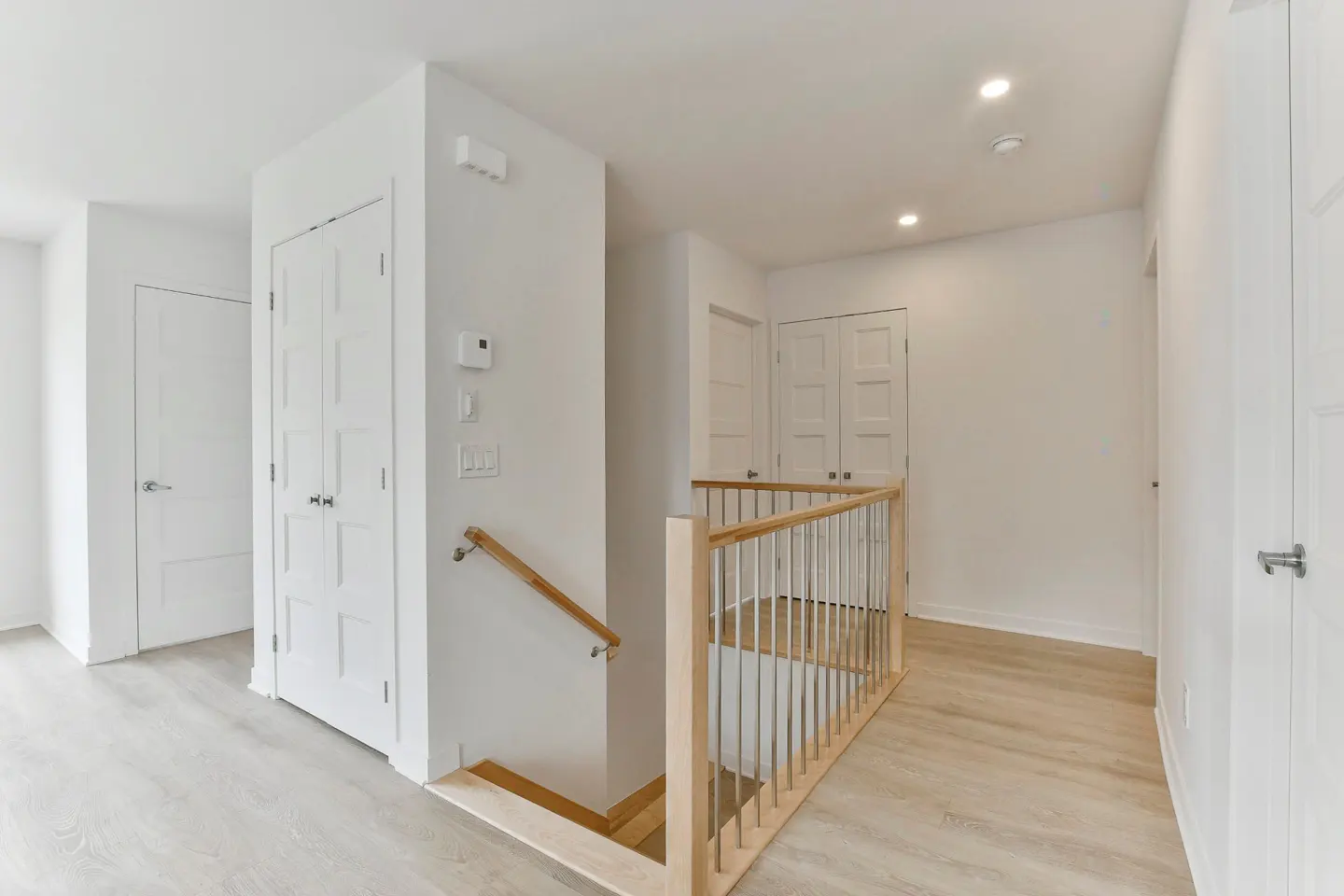 Bright, white hallway with light wood floors, doors, and a staircase with a wood and metal railing.