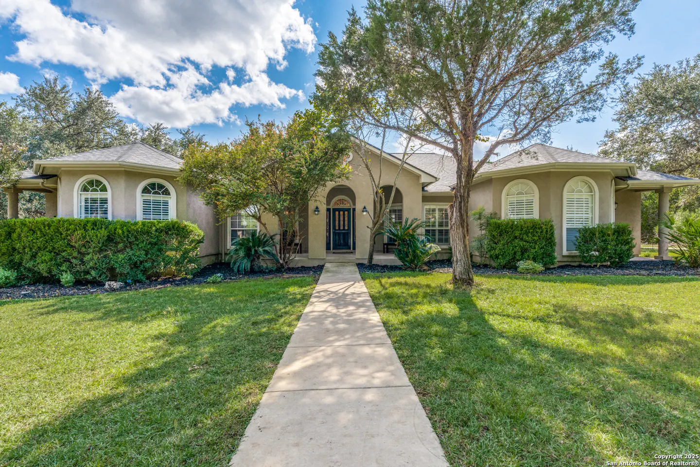 Beige single-story home with a dark blue front door, arched windows, and a green lawn under a partly cloudy sky.