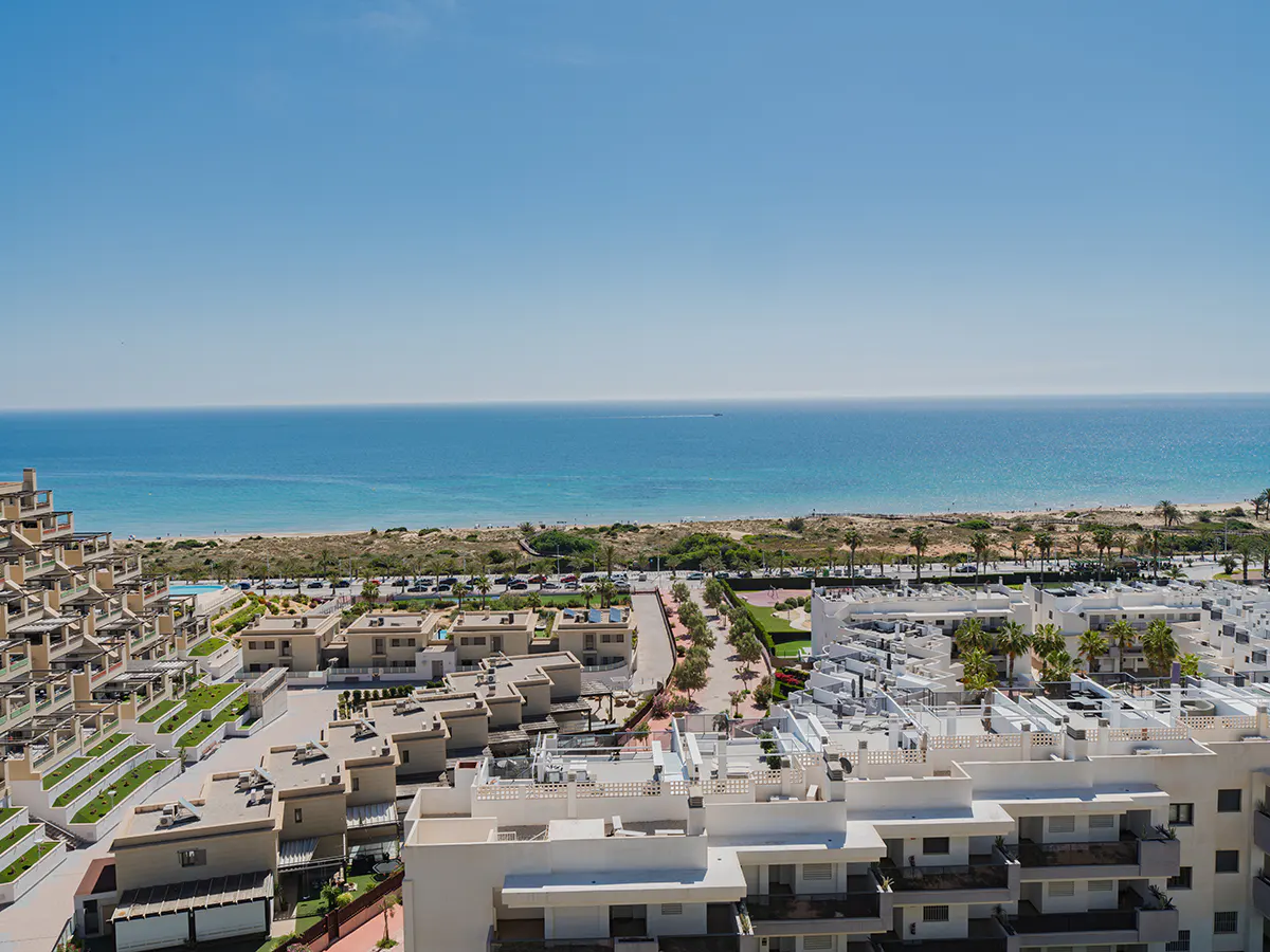 Aerial view of white buildings near a beach and blue ocean under a clear blue sky.