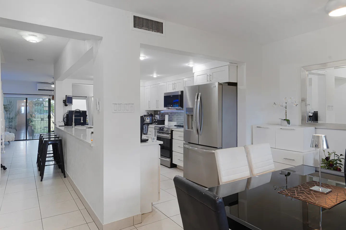 Bright, modern kitchen with white cabinets, stainless steel appliances, and a black dining table with white chairs.