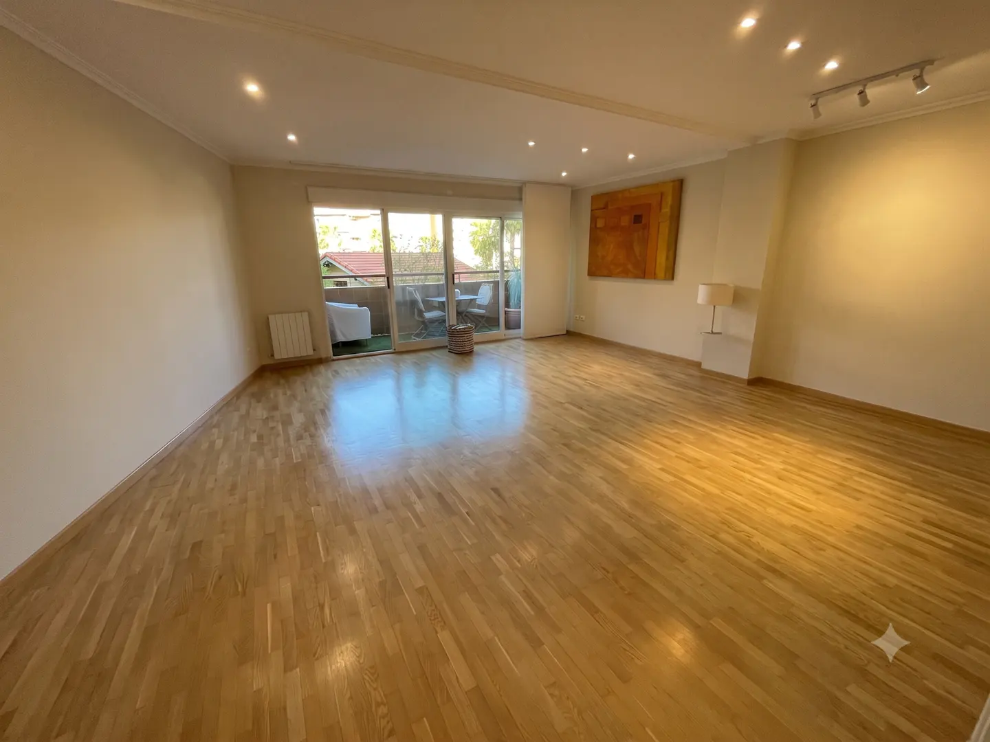 Spacious living room with light wood floors, recessed lighting, large sliding glass doors to a balcony, and wall art.