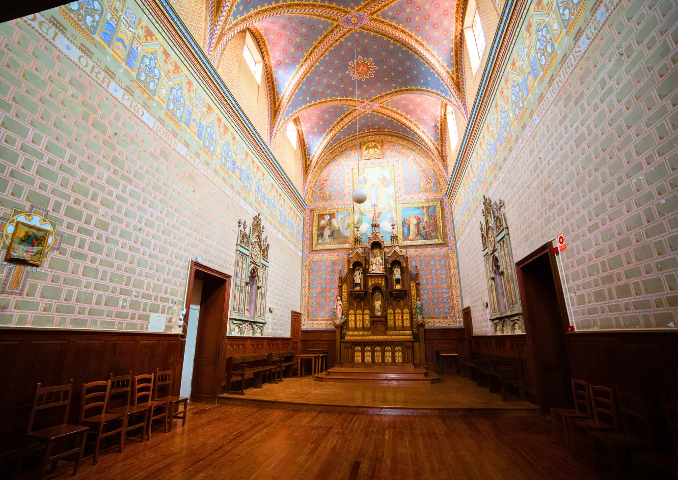Interior view of a church with a wooden altar, paintings, and a blue and pink patterned ceiling.