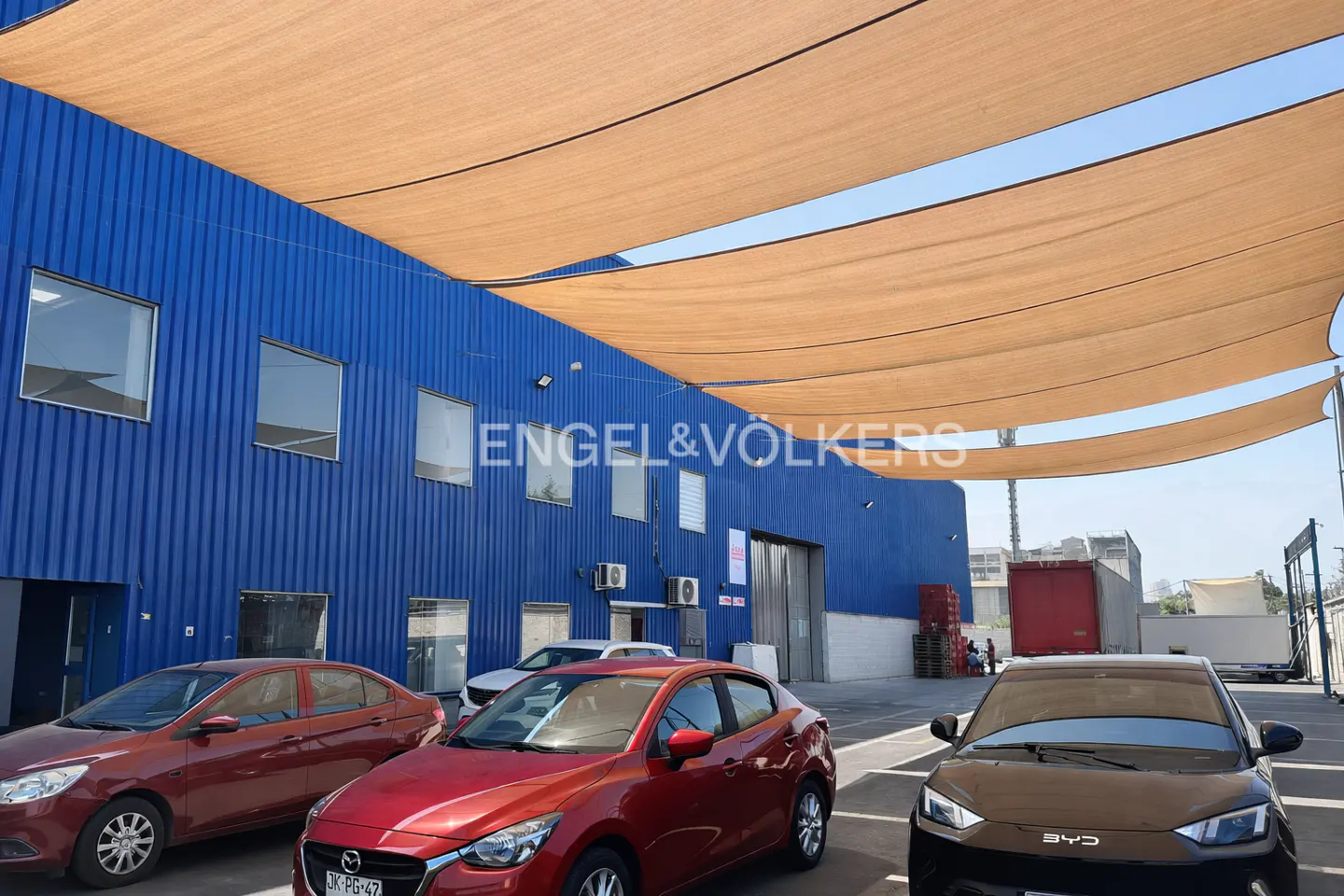 Exterior of a blue Engel & Völkers building with cars parked in front and tan shade sails overhead.