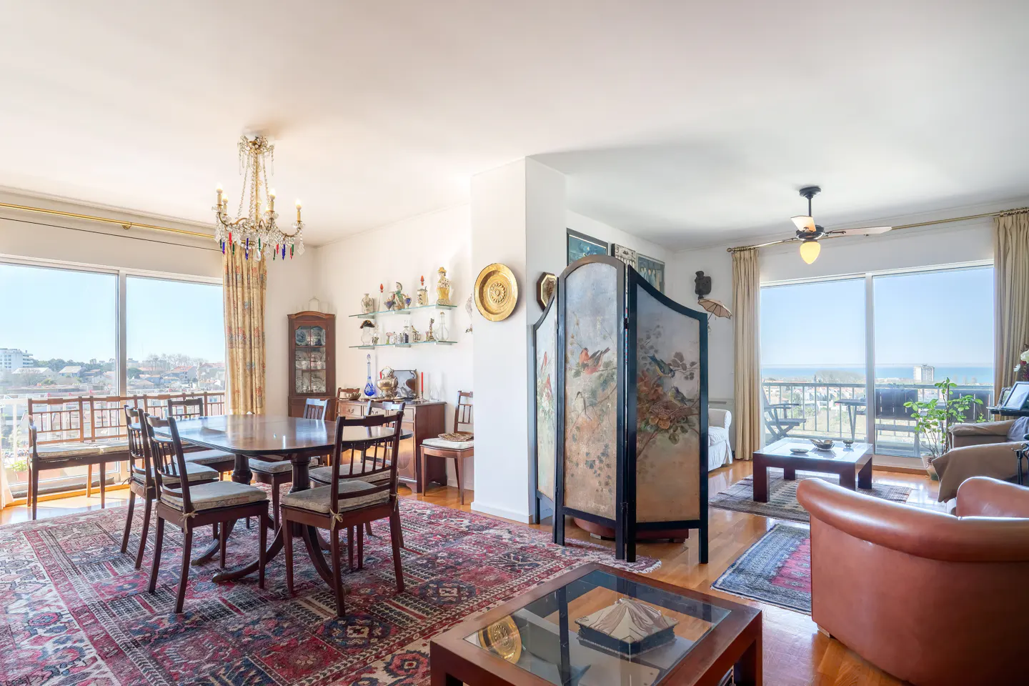 Bright, open-concept living and dining area with hardwood floors, a red patterned rug, and large windows with city views. A decorative screen separates the spaces.