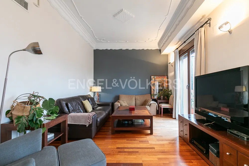 Living room with hardwood floors, a brown leather sofa, a beige sofa, and a dark gray accent wall. A large TV sits on a wooden console.