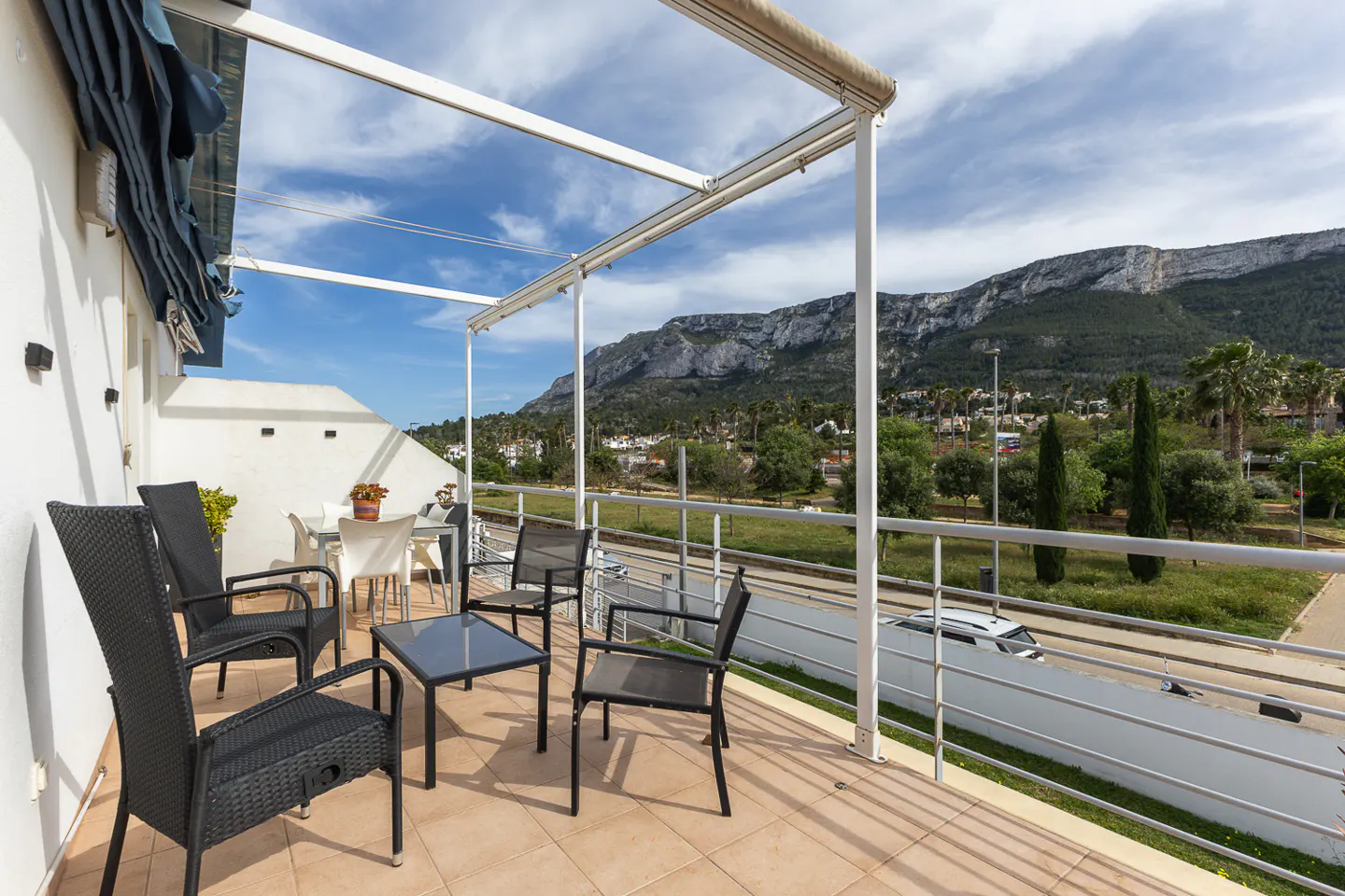 Outdoor patio with black wicker chairs, a glass table, and a white metal pergola overlooking a mountain range.
