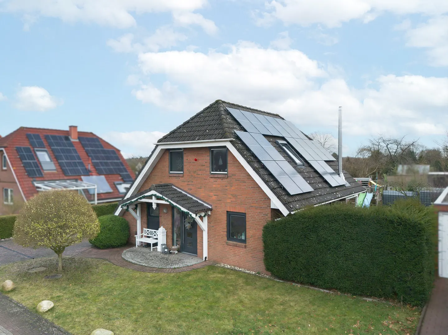 A two-story brick house with solar panels on the roof, a green lawn, and a cloudy sky.