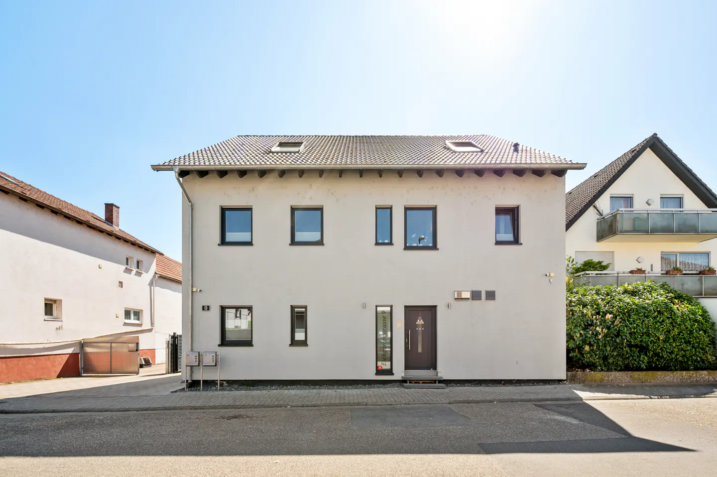 Two-story white house with a brown door and black framed windows under a clear blue sky.