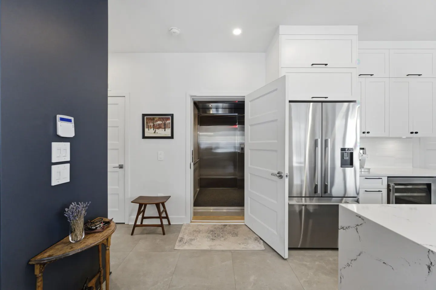 A modern kitchen with white cabinets, stainless steel appliances, and an open elevator.