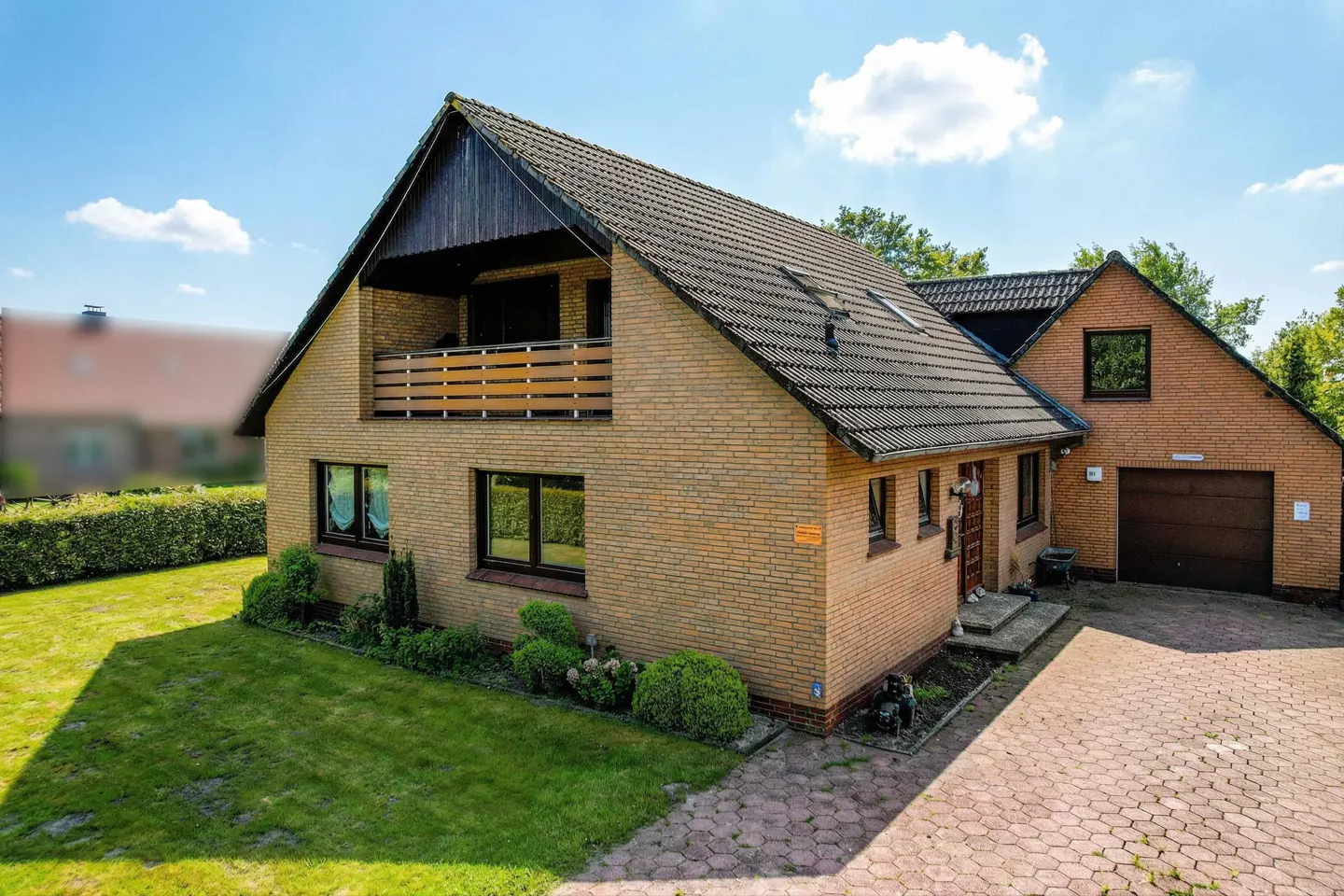 Two-story brick house with a dark roof, balcony, and attached garage on a sunny day.