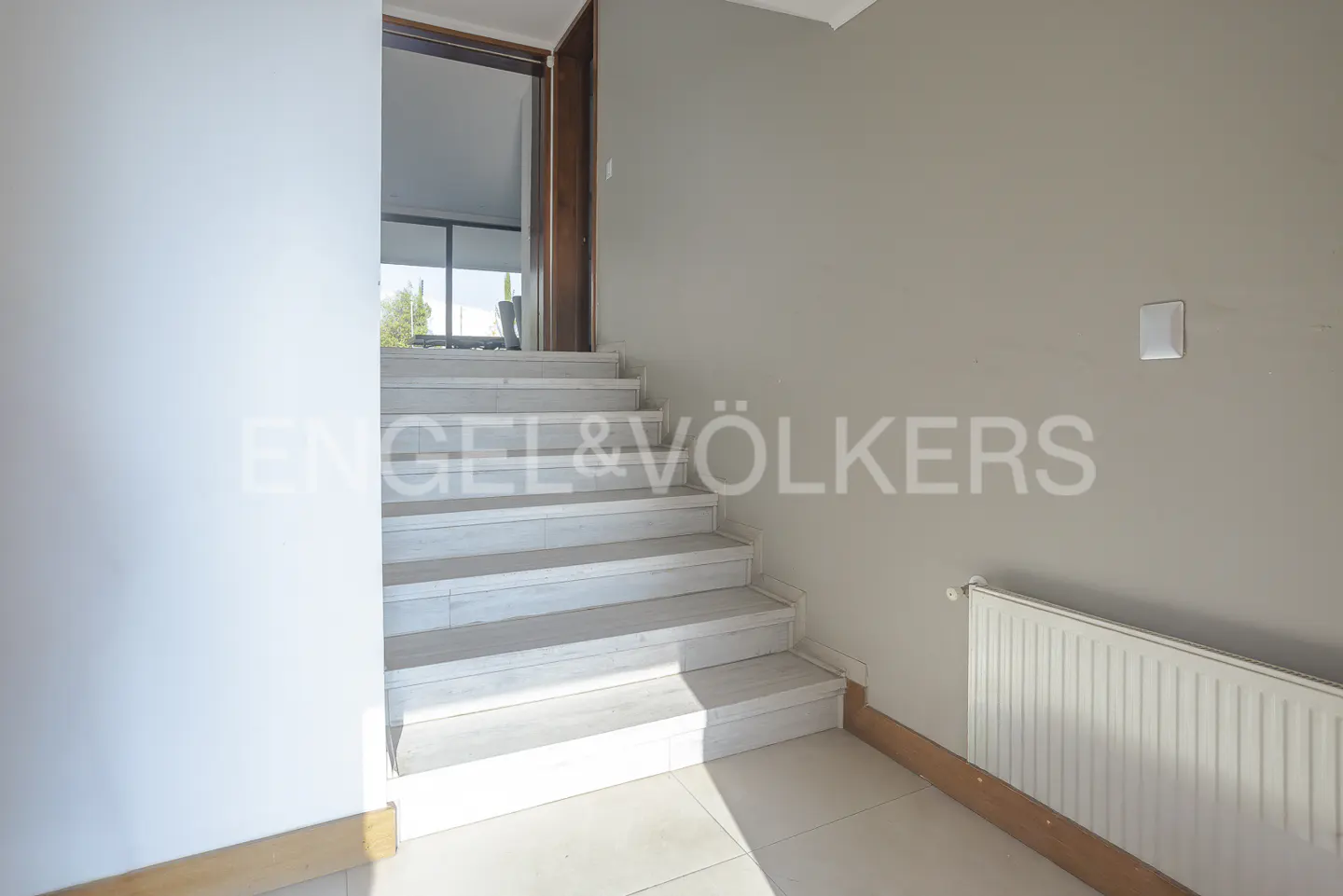 Interior view of a staircase with white steps, leading to a doorway with a brown frame. A white radiator is on the right wall.